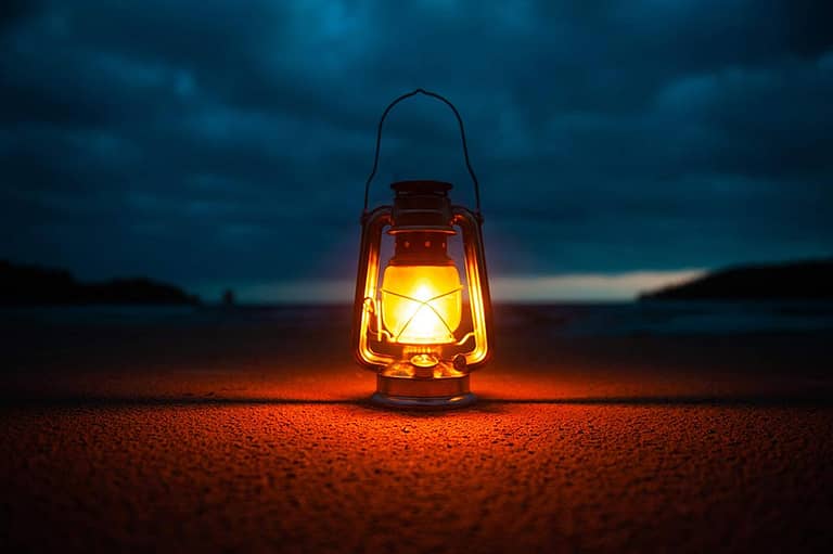 a bright lantern sits on a beach at dusk