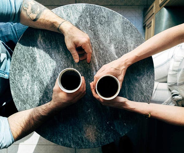 two sets of hands holding coffee cups are seen from above