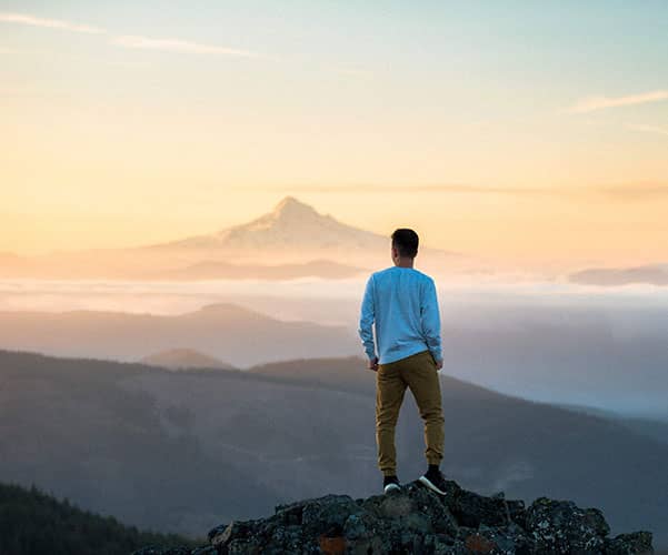 a young man stands on top of a mountain overlooking a vast scenery