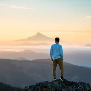 a young man stands on top of a mountain overlooking a vast scenery